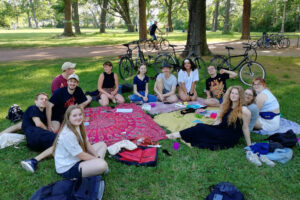 Eine Gruppe junger Personen sitzt im Kreis auf einer Wiese und schaut in die Kamera.