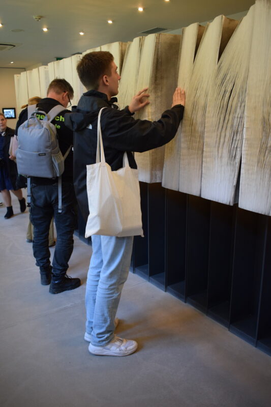 Junge Personen blättern durch große Papier-Bahnen mit Namen.