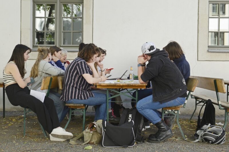 Eine Gruppe Personen sitzt um einen Tisch herum. Die Perosnen schrieben und sprechen miteinander.