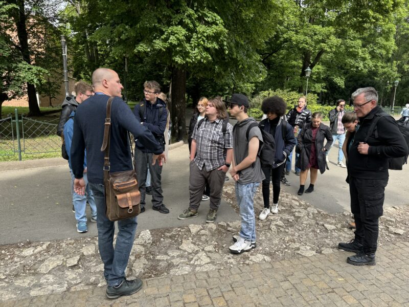 Junge Personen stehen vor einer Person die gestikuliert.